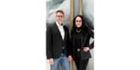 Mann und Frau in schwarzer Businesskleidung stehen nebeneinander vor modernem Hintergrund.