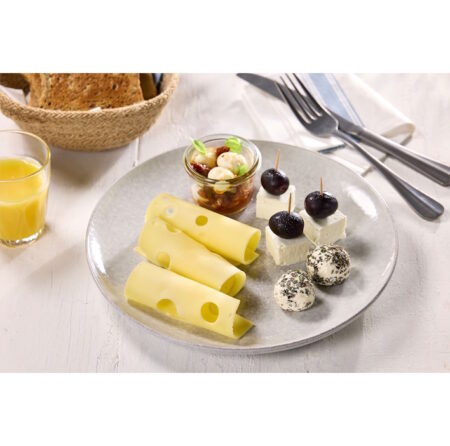 Mit der Käsevielfalt von Lactalis Foodservice Deutschland Umsatzpotenziale gezielt nutzen Cheese platter with rolled Swiss cheese, cheese cubes topped with olives, herb-coated cheese balls, a jar of marinated nuts, plus bread and orange juice in the background.